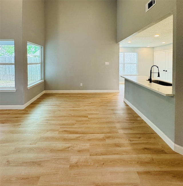 empty room featuring a sink, a towering ceiling, healthy amount of natural light, light wood-style flooring, and baseboards