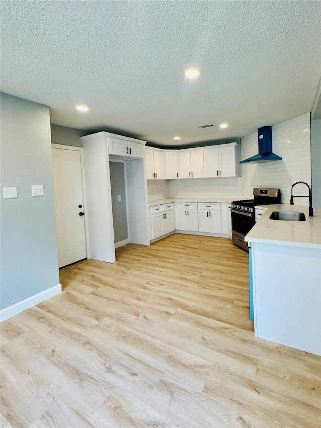 kitchen with stainless steel gas range, wall chimney exhaust hood, a sink, tasteful backsplash, and white cabinets