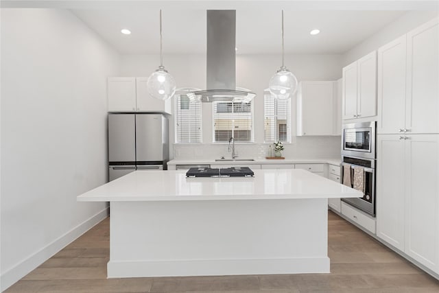 kitchen featuring appliances with stainless steel finishes, island range hood, a kitchen island, a sink, and light wood-style floors