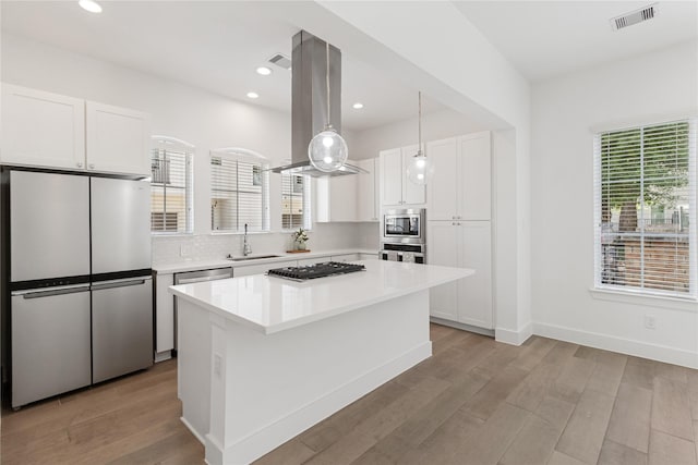 kitchen featuring stainless steel appliances, a sink, island exhaust hood, white cabinetry, and recessed lighting