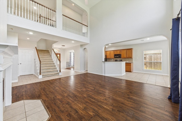 15127 Woodford Hollow Ln, Cypress, TX 77429 - unfurnished living room with arched walkways, light wood finished floors, a high ceiling, plenty of natural light, and stairway
