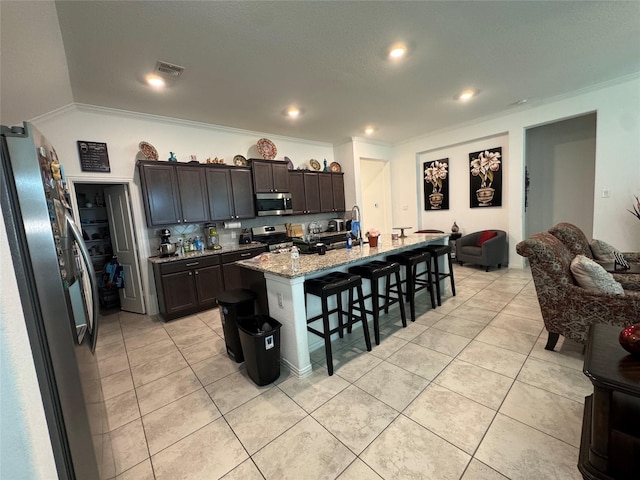 13510 Dovetail Canyon Ct, Rosharon, TX 77583 - kitchen featuring appliances with stainless steel finishes, ornamental molding, a kitchen bar, light tile patterned floors, and an island with sink