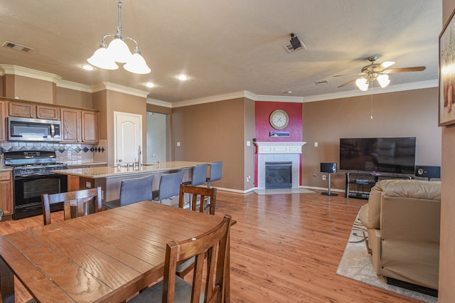 dining space with ceiling fan, baseboards, ornamental molding, light wood-style floors, and a tiled fireplace