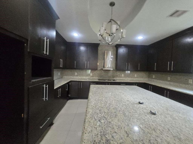 kitchen featuring wall chimney exhaust hood, backsplash, light tile patterned flooring, a chandelier, and light stone counters