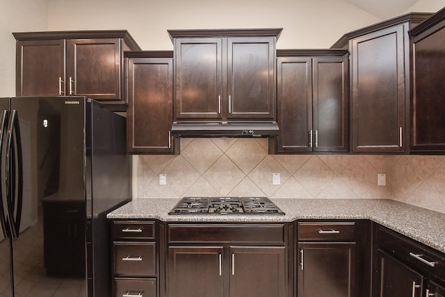 kitchen with gas cooktop, under cabinet range hood, freestanding refrigerator, backsplash, and dark brown cabinets