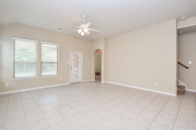 unfurnished room featuring arched walkways, ceiling fan, stairway, lofted ceiling, and light tile patterned floors