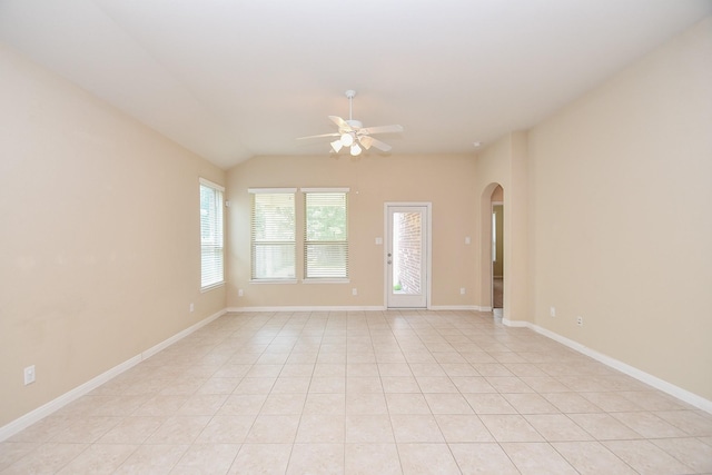 spare room featuring arched walkways, ceiling fan, vaulted ceiling, light tile patterned flooring, and baseboards
