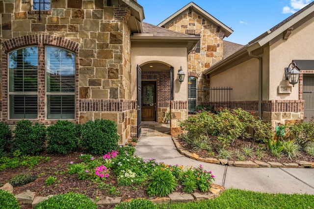 property entrance with stone siding, stucco siding, and fence