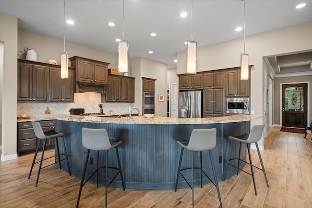 kitchen with appliances with stainless steel finishes, a large island with sink, backsplash, light wood-type flooring, and recessed lighting
