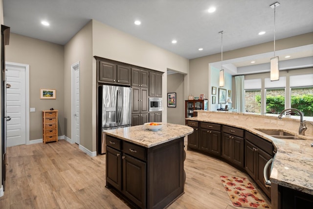 kitchen featuring a sink, appliances with stainless steel finishes, light wood finished floors, dark brown cabinets, and light stone counters