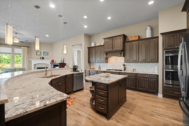 kitchen with appliances with stainless steel finishes, dark brown cabinets, open floor plan, a sink, and recessed lighting