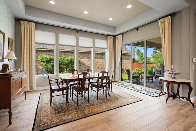 dining area with a raised ceiling, light wood-style flooring, recessed lighting, and baseboards