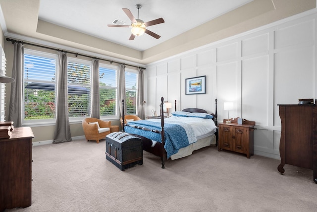 bedroom with a decorative wall, light carpet, multiple windows, and ceiling fan