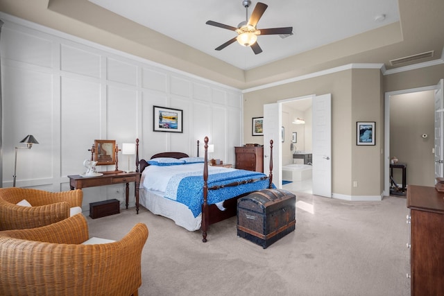 bedroom with light carpet, a tray ceiling, a decorative wall, ceiling fan, and ensuite bathroom