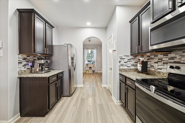 21022 Solstice Point Dr, Hockley, TX 77447 - kitchen featuring appliances with stainless steel finishes, arched walkways, light wood-style flooring, dark brown cabinets, and tasteful backsplash