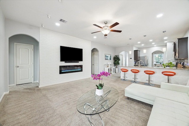 21022 Solstice Point Dr, Hockley, TX 77447 - living room with arched walkways, ceiling fan, light colored carpet, a glass covered fireplace, and recessed lighting