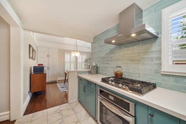 kitchen with wall chimney range hood, stainless steel appliances, light countertops, and decorative backsplash