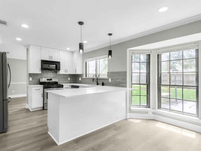kitchen with black microwave, gas range, freestanding refrigerator, light wood-type flooring, and recessed lighting