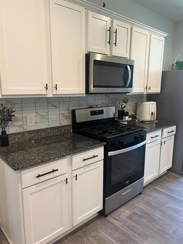 kitchen with appliances with stainless steel finishes, wood finished floors, white cabinets, and backsplash