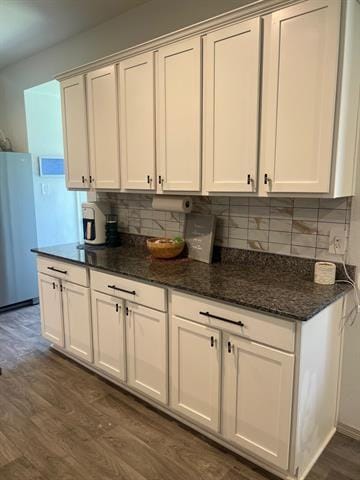 kitchen featuring dark wood finished floors, decorative backsplash, freestanding refrigerator, dark stone countertops, and white cabinetry