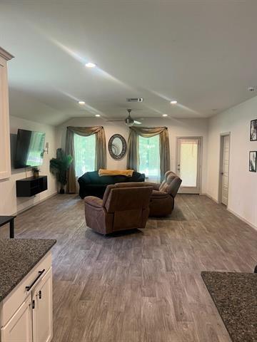 living room with plenty of natural light, wood finished floors, a ceiling fan, baseboards, and vaulted ceiling