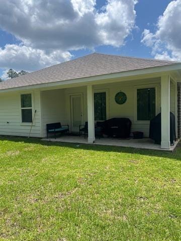 back of house with a yard, a patio, and roof with shingles