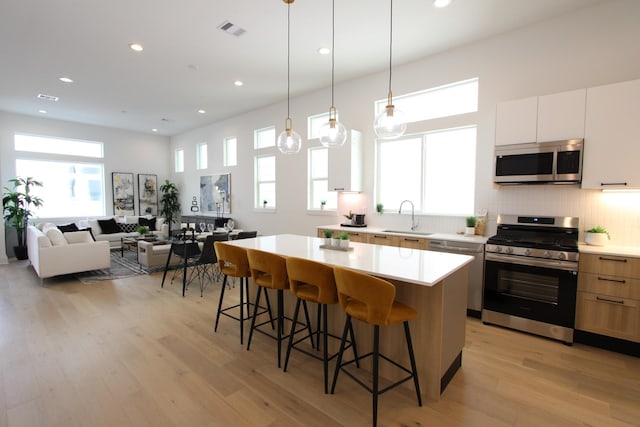 kitchen with appliances with stainless steel finishes, a sink, a kitchen island, a kitchen bar, and light countertops