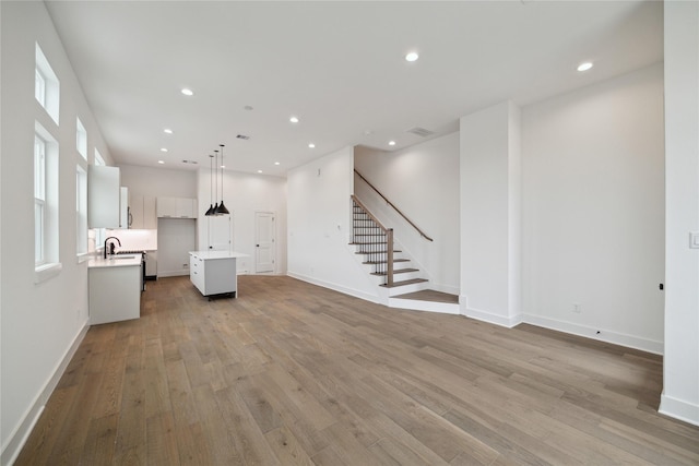 unfurnished living room with light wood-type flooring, a sink, stairs, baseboards, and recessed lighting
