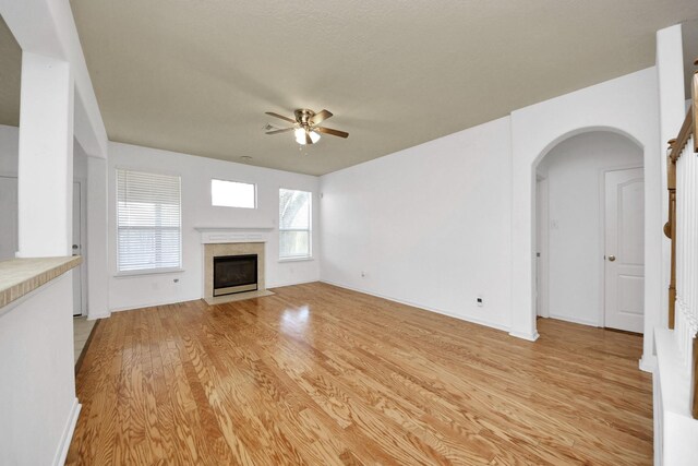 13114 Oak Ledge Dr, Houston, TX 77065 - unfurnished living room with arched walkways, ceiling fan, light wood finished floors, a fireplace with flush hearth, and baseboards