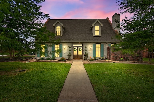 cape cod-style house with french doors, a chimney, a yard, and a shingled roof
