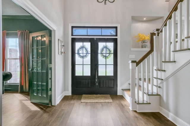 foyer entrance with healthy amount of natural light, wood finished floors, stairway, french doors, and a high ceiling