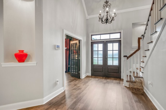 entrance foyer featuring french doors, wood finished floors, ornamental molding, stairs, and a chandelier