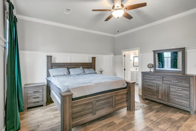 bedroom with crown molding, wood finished floors, a wainscoted wall, ceiling fan, and ensuite bathroom