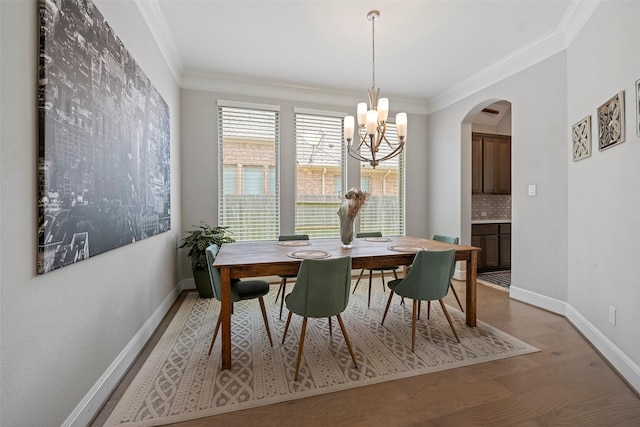 dining space with a chandelier, ornamental molding, wood finished floors, arched walkways, and baseboards