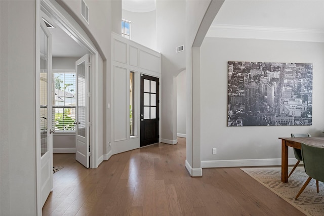 foyer entrance featuring plenty of natural light, arched walkways, wood finished floors, baseboards, and crown molding