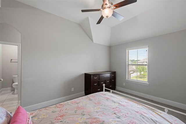 bedroom featuring baseboards, ensuite bath, vaulted ceiling, and a ceiling fan