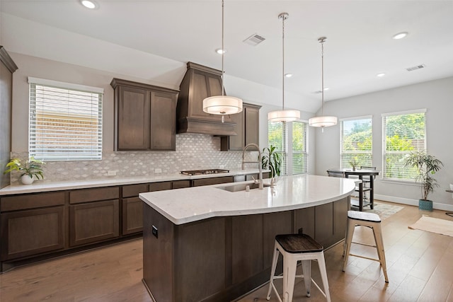 kitchen featuring a sink, custom exhaust hood, stainless steel gas cooktop, light wood-style flooring, and tasteful backsplash