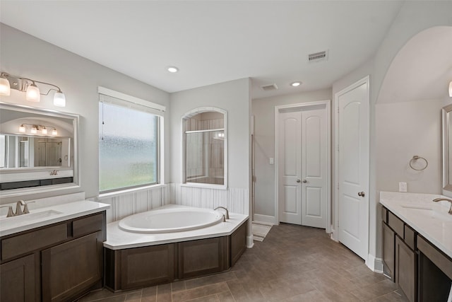 bathroom featuring a stall shower, a garden tub, two vanities, and recessed lighting
