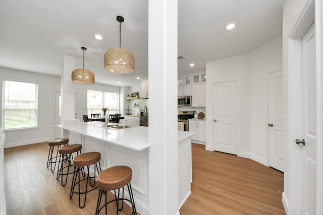 2003 Ballesteros St, Crosby, TX 77532 - kitchen featuring appliances with stainless steel finishes, light wood-style floors, a sink, a breakfast bar area, and white cabinetry