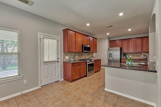 kitchen with stainless steel appliances, decorative backsplash, dark stone countertops, a sink, and recessed lighting