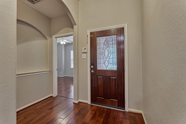 foyer entrance featuring arched walkways, dark wood-style flooring, a textured wall, and baseboards