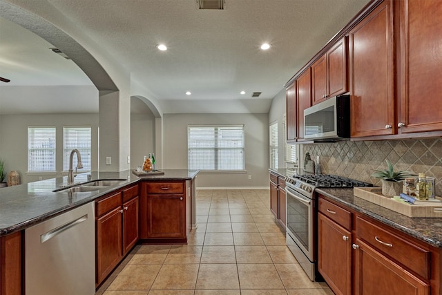 kitchen featuring stainless steel appliances, a sink, baseboards, tasteful backsplash, and dark stone countertops