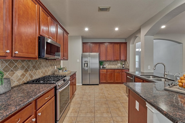 kitchen featuring appliances with stainless steel finishes, a sink, arched walkways, decorative backsplash, and dark stone counters