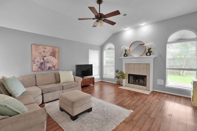 living area with wood finished floors, a ceiling fan, a tile fireplace, vaulted ceiling, and baseboards