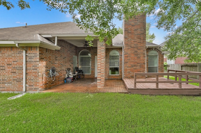 rear view of house featuring a chimney, a deck, brick siding, roof with shingles, and a patio