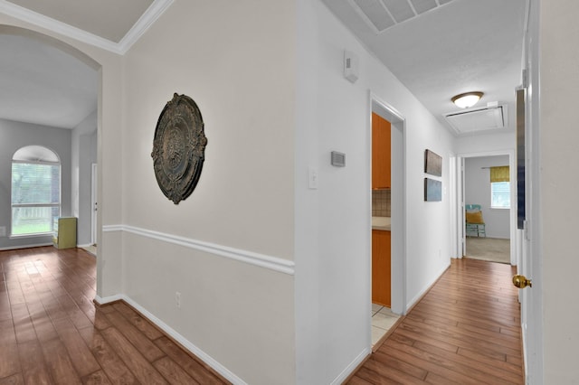 corridor featuring light wood-type flooring, plenty of natural light, baseboards, arched walkways, and crown molding