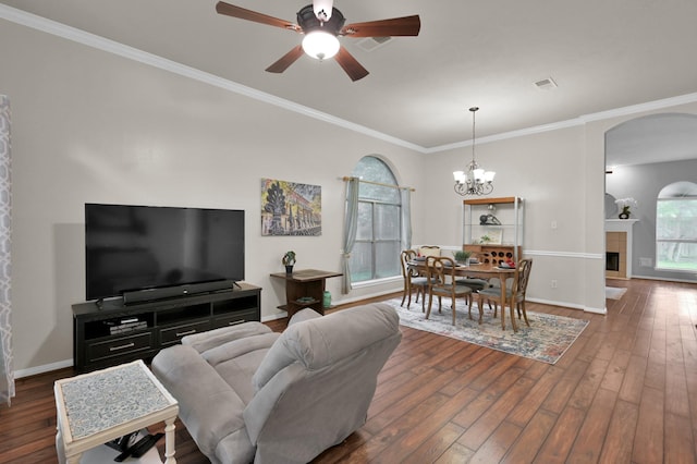 living room with arched walkways, dark wood-style floors, a ceiling fan, crown molding, and a tiled fireplace