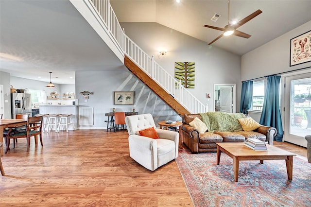 living area with light wood finished floors, stairs, a ceiling fan, and high vaulted ceiling