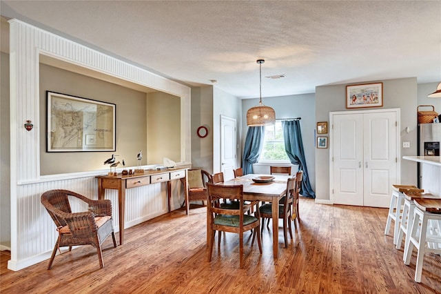 dining area with light wood finished floors, a textured ceiling, and baseboards