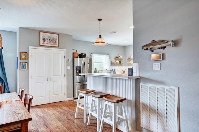 kitchen featuring stainless steel fridge with ice dispenser, light wood-type flooring, a breakfast bar area, pendant lighting, and a peninsula